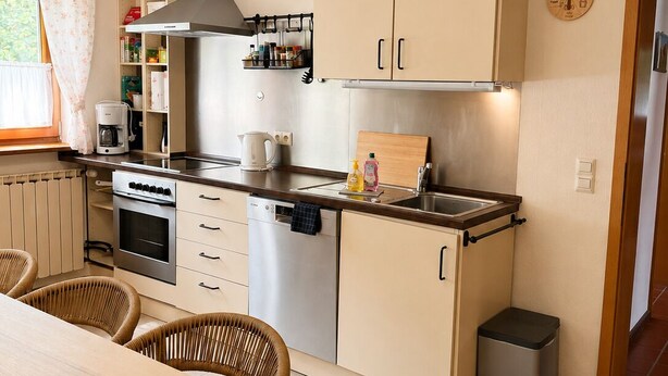 Une cuisine compacte avec un coin repas, comprenant une cuisinière, un four, un lave-vaisselle et une petite poubelle.