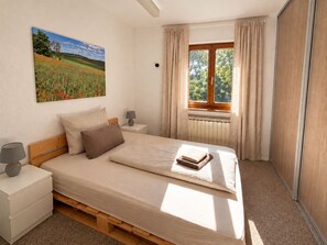 A bedroom with a bed, bedside tables, a window with curtains, a radiator, and a painting on the wall.