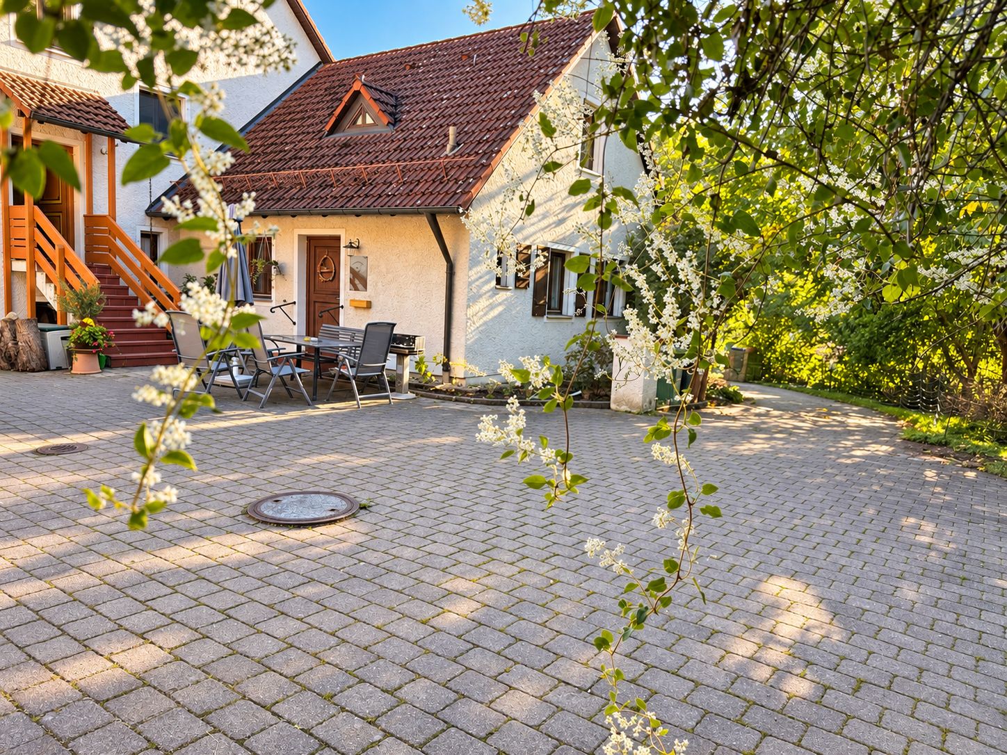 A courtyard with a paved patio, a dining area with outdoor furniture, and a building with a sloped roof.