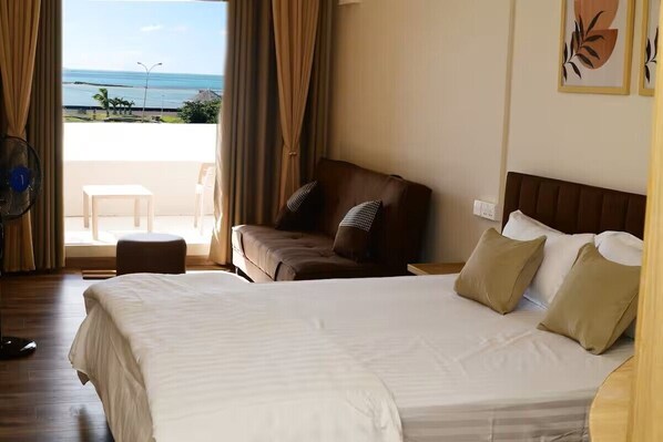 A hotel room with a bed, a chair, a small table, and a view of the beach.