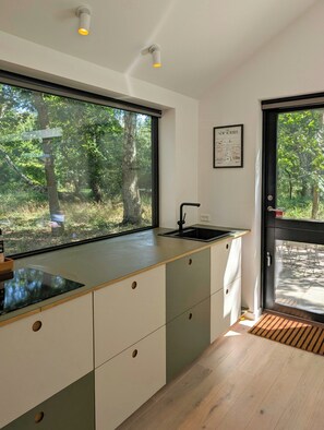 Eine moderne Küche mit einem großen Fenster, einer Spüle und einer Tür, die nach draußen führt.