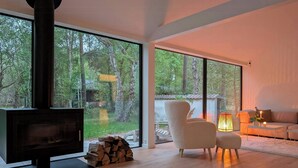 En moderne stue med en stor pejs, en behagelig sofa og udsigt til en skov gennem store vinduer.
