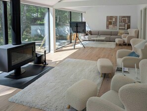 A modern living room with a fireplace, large windows, a sofa, and a white fluffy rug. - Modern oasis in the middle of the forest in Rørvig (Rørvig)