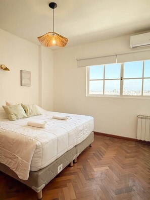 Un dormitorio con cama, ventana, radiador y lámpara colgante.