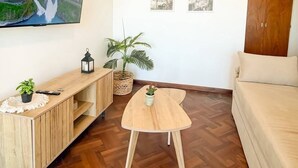 Un soggiorno con un'ampia TV a schermo piatto montata a parete, un mobile TV in legno, un tavolino rotondo, un divano beige e due quadri appesi.
