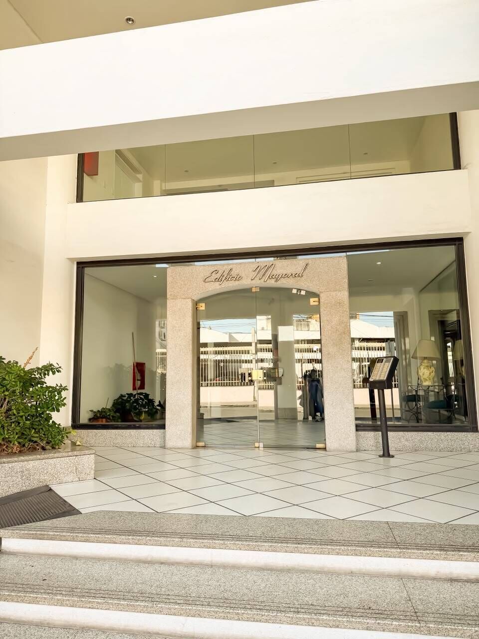 Une entrée moderne avec une façade en verre, un ciel dégagé visible à travers les fenêtres et une enseigne indiquant « Edificio Mayoral ».