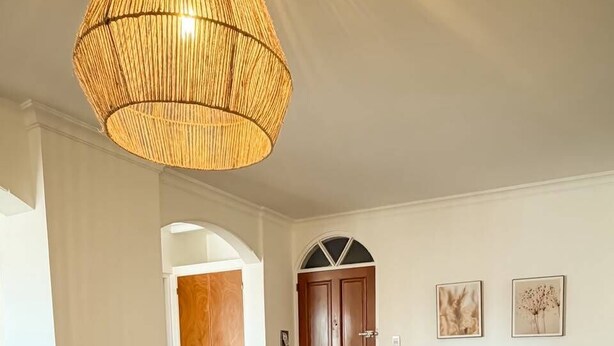 Zona pranzo con tavolo e sedie bianche, un lampadario intrecciato e una porta in legno sullo sfondo.