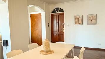 A dining area with a white table and chairs, a woven light fixture, and a wooden door in the background.
