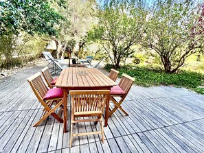 Eine hölzerne Terrasse im Freien mit Tisch und Stühlen, umgeben von Grünpflanzen.