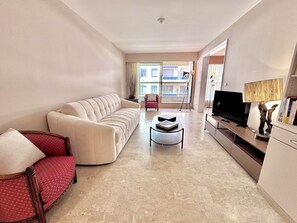 Un salon moderne comprenant un canapé, un fauteuil, une table basse, un téléviseur et des objets de décoration.