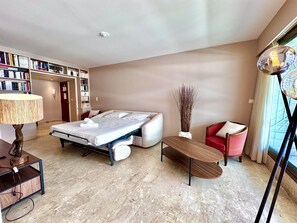 Ein Hotelzimmer mit einem Bett, einem Schreibtisch, einem Stuhl, einem Bücherregal und einem großen Fenster.