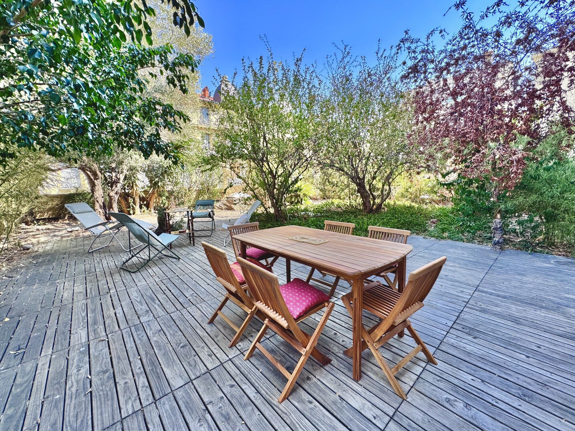 An outdoor wooden deck with a table and chairs, surrounded by trees and greenery.