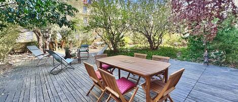 An outdoor wooden deck with a table and chairs, surrounded by trees and greenery.