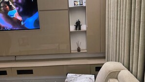 A living room with a flat-screen TV mounted on the wall, a beige sofa, and a decorative light fixture. - A premium apartment in the heart of Ibadan, offering comfort and convenience. (Ibadan)