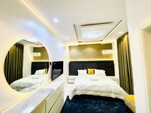 Una habitación de hotel moderna con una cama grande, un espejo redondo y un escritorio empotrado.
