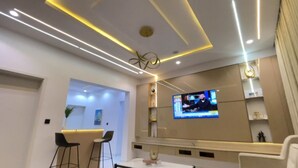 A modern living room with a flat-screen TV mounted on the wall, a ceiling with linear lighting, and a seating area with two chairs. - A premium apartment in the heart of Ibadan, offering comfort and convenience. (Ibadan)