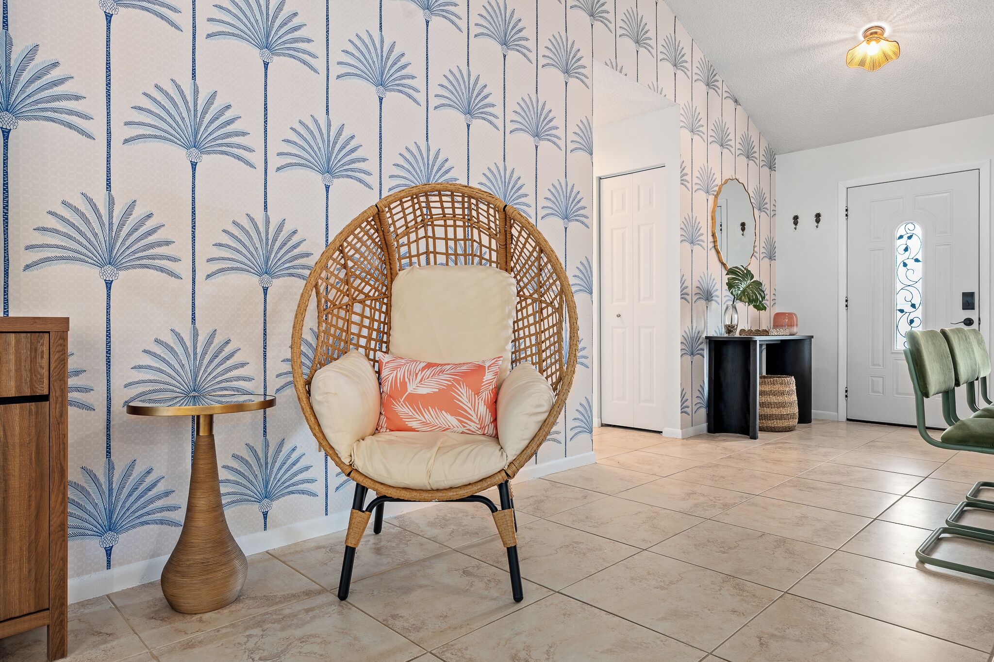 Um quarto com uma cadeira de vime, uma mesa redonda pequena e uma parede estampada.