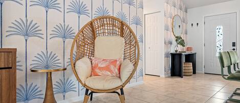 Une pièce avec un fauteuil en osier, une petite table ronde et un mur orné de motifs.