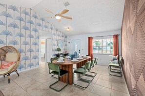 Een eetgedeelte met een ronde houten tafel, groene stoelen en een plafondventilator.