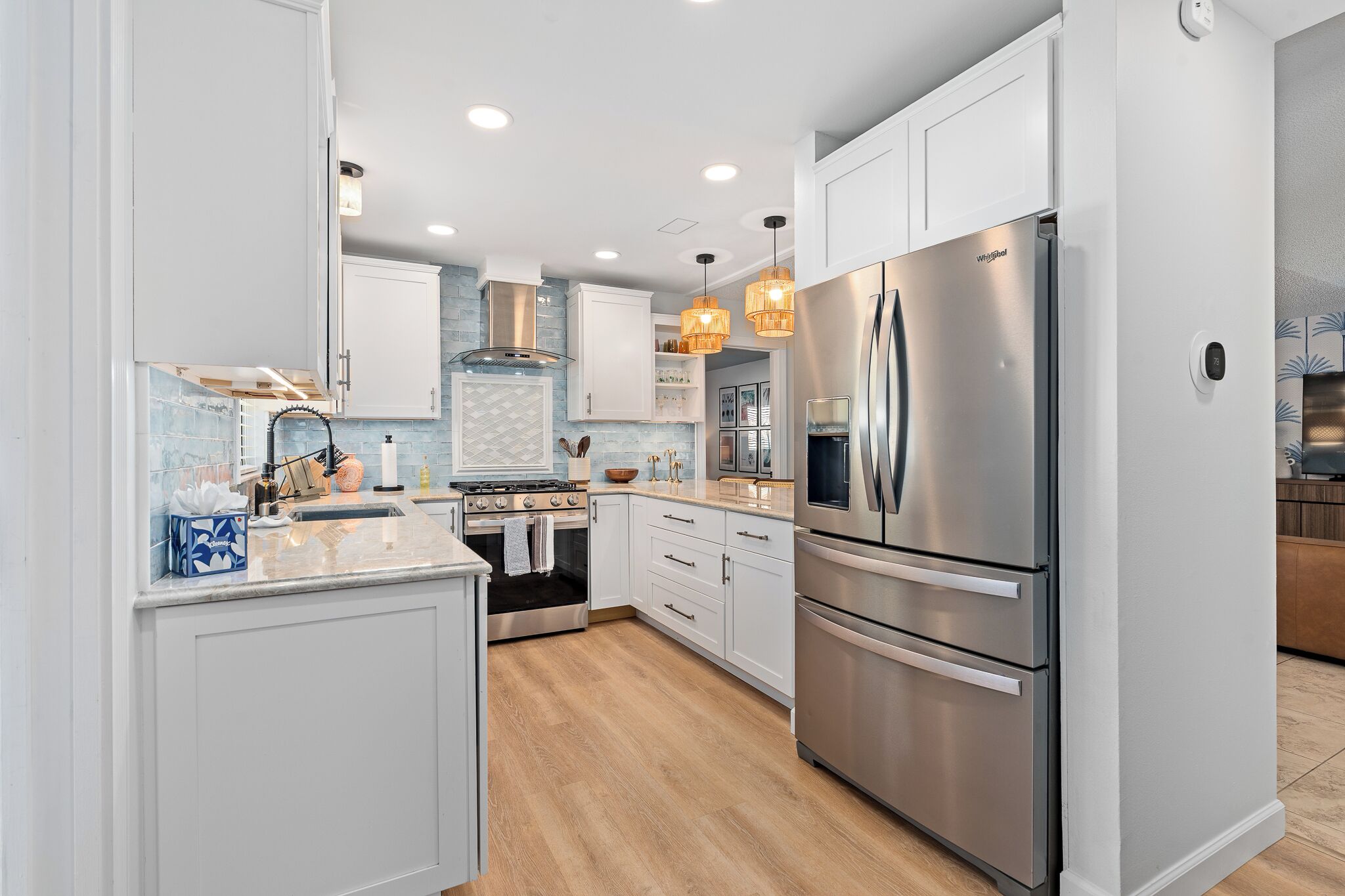 A modern kitchen with stainless steel appliances, white cabinetry, and a wooden floor.