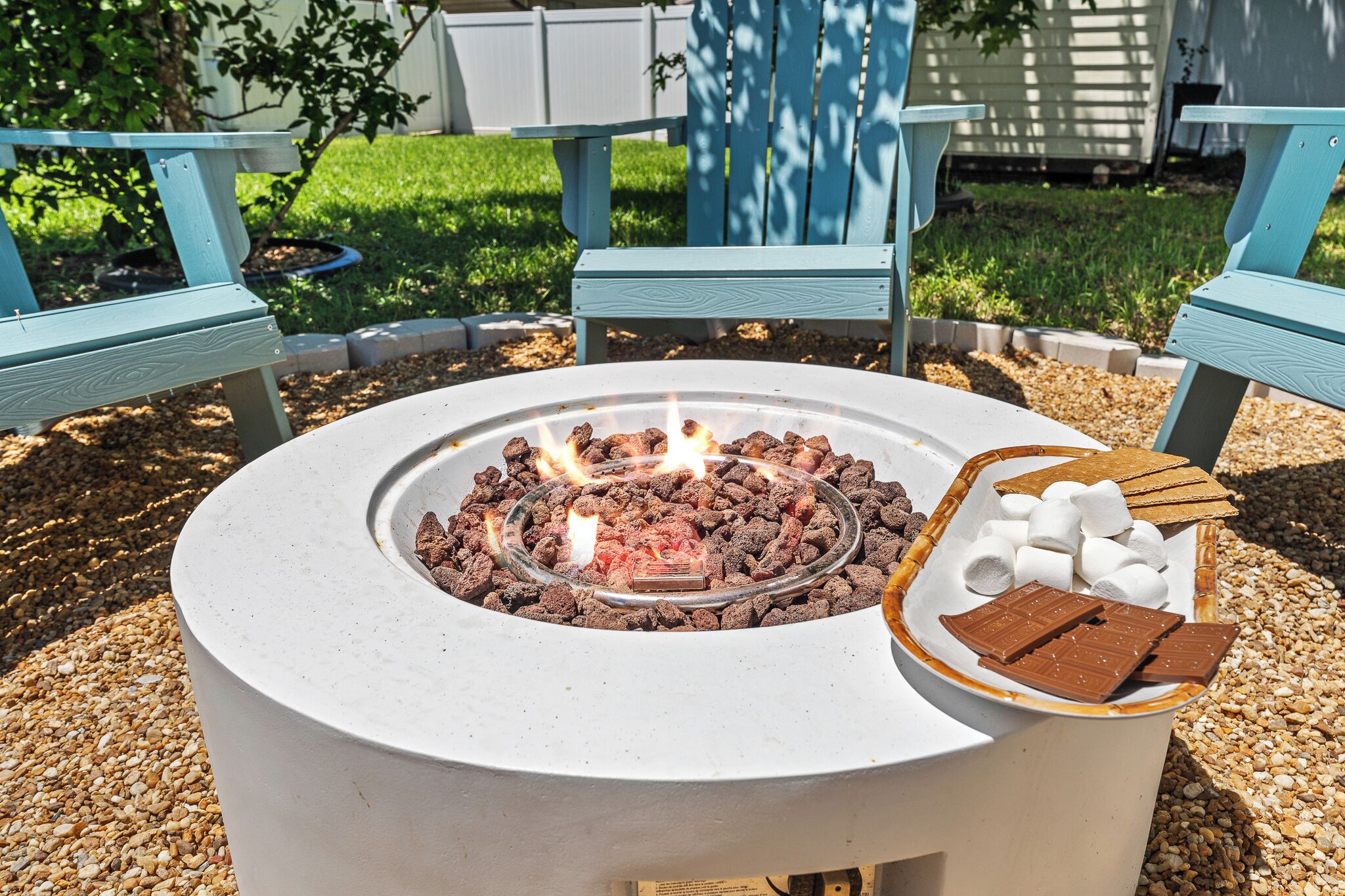 A round outdoor fire pit with burning wood, surrounded by a gravel area.