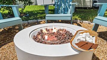 A round outdoor fire pit with burning wood, surrounded by a gravel area.