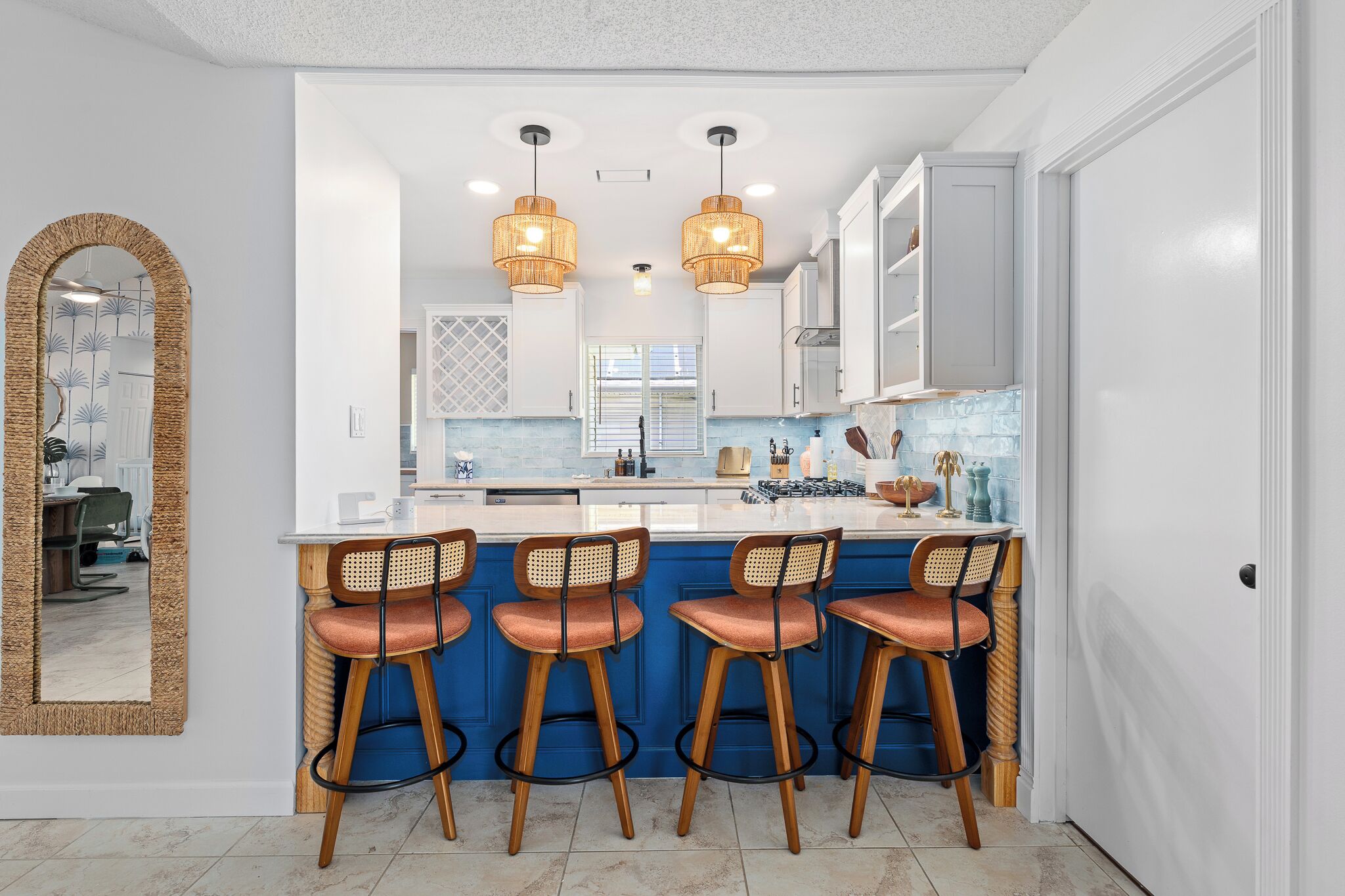 A kitchen with a central island, bar stools, pendant lights, and a large mirror.