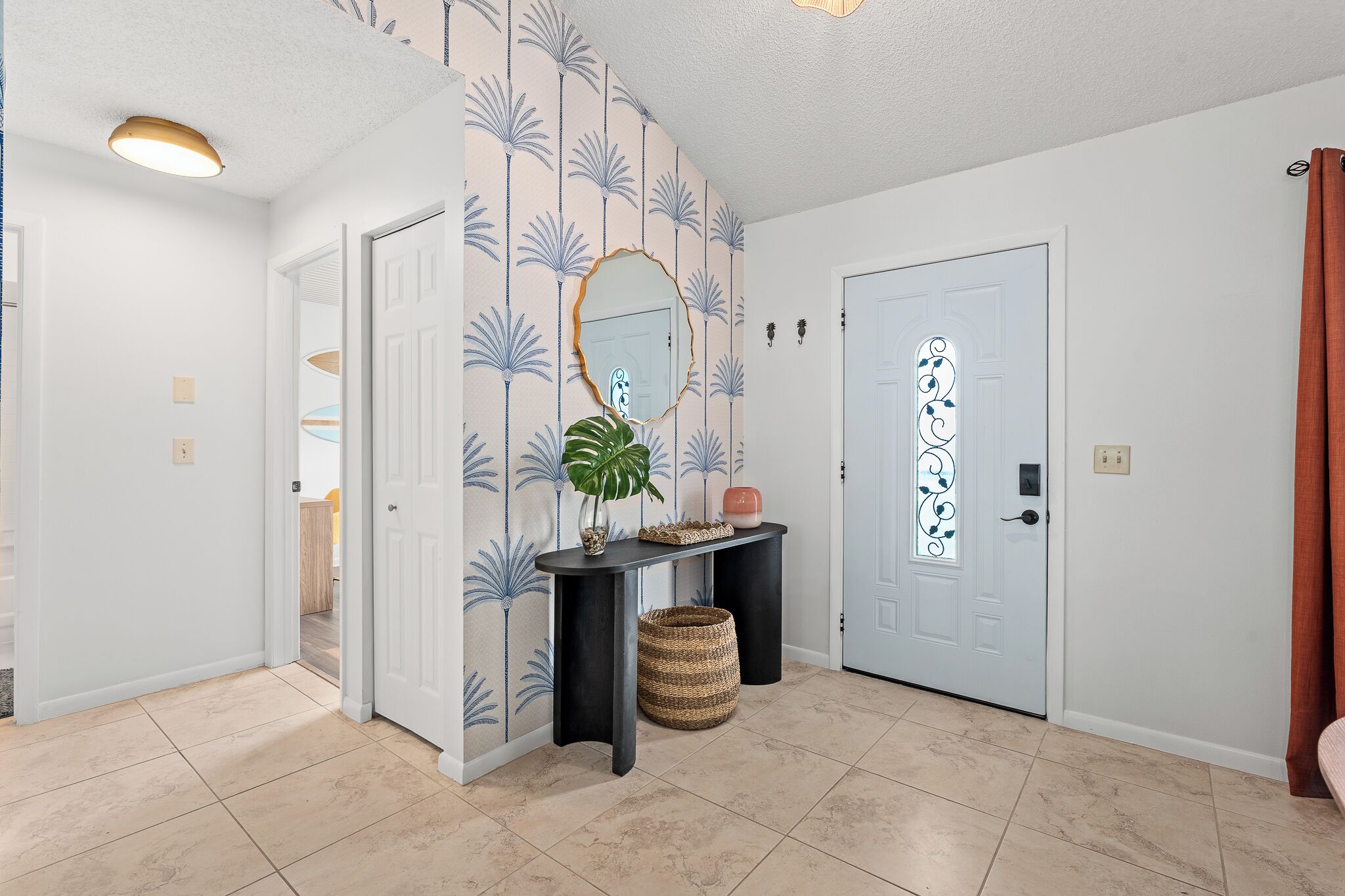 A hallway with a white door, a mirror, a console table with a plant, and a decorative door with a swirl pattern.