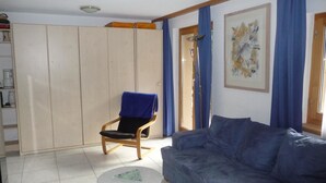 A living room with a blue sofa, a chair with a blue cover, a small round table, and a wardrobe. - Chalet Solana 1 # 2-bed apartment, Bad, WC 2-Bettwohnung, Bad, WC by Interhome (Leukerbad)