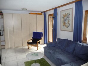A living room with a blue sofa, a chair with a blue cover, a small round table, and a wardrobe. - Chalet Solana 1 # 2-bed apartment, Bad, WC 2-Bettwohnung, Bad, WC by Interhome (Leukerbad)