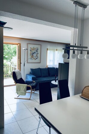 A modern living room with a sofa, a dining table, and a chair. There is a painting on the wall and a lamp. - Chalet Solana 1 # 2-bed apartment, Bad, WC 2-Bettwohnung, Bad, WC by Interhome (Leukerbad)