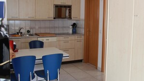 A kitchen with light wooden cabinets, a microwave, and a sink. There is a dining table with blue chairs. - Chalet Solana 1 # 2-bed apartment, Bad, WC 2-Bettwohnung, Bad, WC by Interhome (Leukerbad)