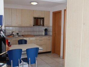 A kitchen with light wooden cabinets, a microwave, and a sink. There is a dining table with blue chairs. - Chalet Solana 1 # 2-bed apartment, Bad, WC 2-Bettwohnung, Bad, WC by Interhome (Leukerbad)