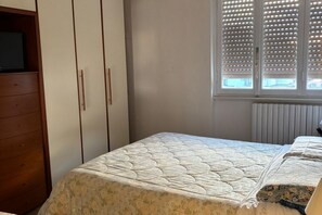 Een slaapkamer met een bed, een dressoir en een raam met zonwering.