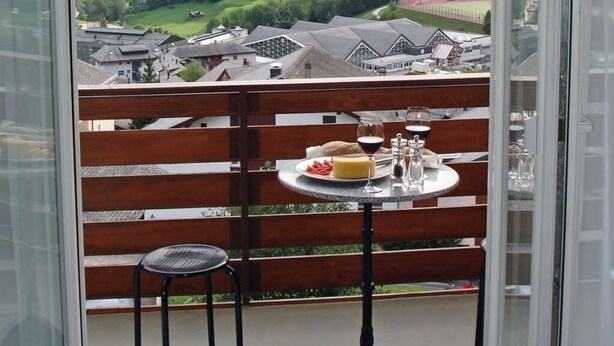 Ein Balkon mit Essplatz, der auf eine Berglandschaft blickt.