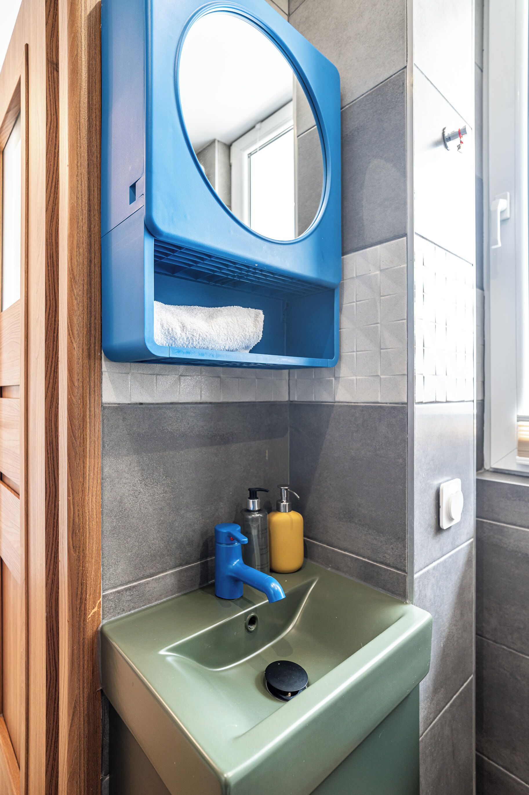 A bathroom with a green sink, a blue faucet, a mirror, and a towel.