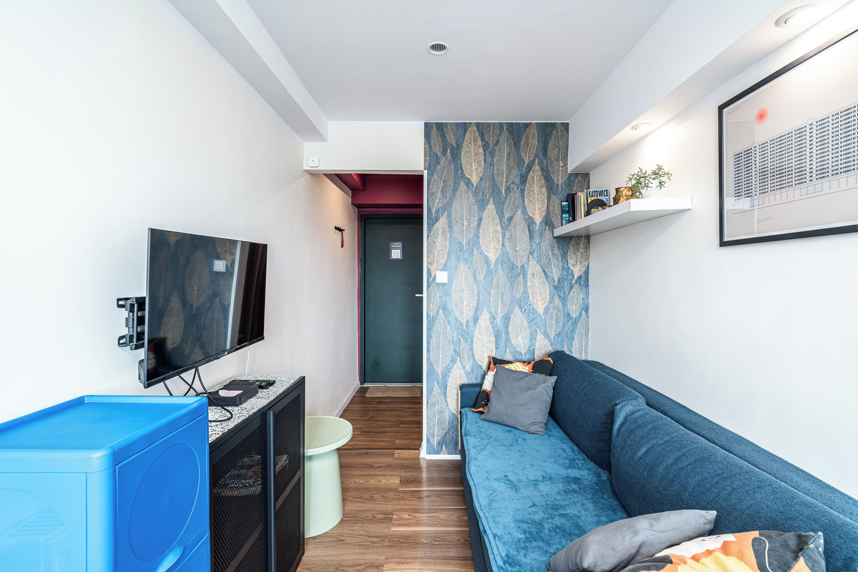 A modern living room with a flat-screen TV, a blue sofa, and a patterned wallpaper.