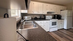 A modern kitchen with white cabinets, a stainless steel sink, a microwave, a stove, and a refrigerator.