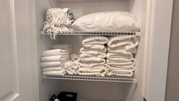 A storage closet with shelves containing folded towels, a first aid kit, and a black container.