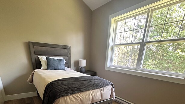 A bedroom with a bed, nightstand, lamp, and a window with a view of trees.