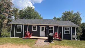 A single-story house with a dark exterior, a front porch with red Adirondack chairs, and a number '1946' on the door.