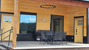 A wooden building with a covered patio area, outdoor seating, and a large window offering a view of the forest. - Duck Creek Cabin near Brian Head, Zion and Bryce Canyon (Duck Creek Village)
