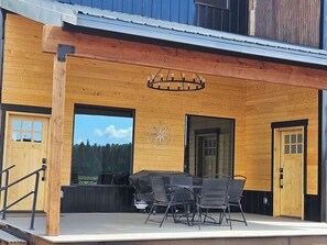A wooden building with a covered patio area, outdoor seating, and a large window offering a view of the forest. - Duck Creek Cabin near Brian Head, Zion and Bryce Canyon (Duck Creek Village)