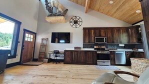 A spacious living area with a wooden ceiling, a mounted television, and a kitchen with dark wooden cabinets and modern appliances. - Duck Creek Cabin near Brian Head, Zion and Bryce Canyon (Duck Creek Village)