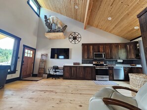 A spacious living area with a wooden ceiling, a mounted television, and a kitchen with dark wooden cabinets and modern appliances. - Duck Creek Cabin near Brian Head, Zion and Bryce Canyon (Duck Creek Village)