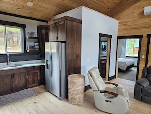 A modern kitchen with a stainless steel refrigerator, a dining area with a leather chair, and a visible laundry room. - Duck Creek Cabin near Brian Head, Zion and Bryce Canyon (Duck Creek Village)