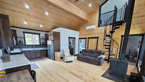 A spacious living area with a wooden floor, a sofa, a dining table, and a kitchen area with a refrigerator and cabinets. - Duck Creek Cabin near Brian Head, Zion and Bryce Canyon (Duck Creek Village)