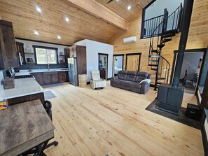 A spacious living area with a wooden floor, a sofa, a dining table, and a kitchen area with a refrigerator and cabinets. - Duck Creek Cabin near Brian Head, Zion and Bryce Canyon (Duck Creek Village)