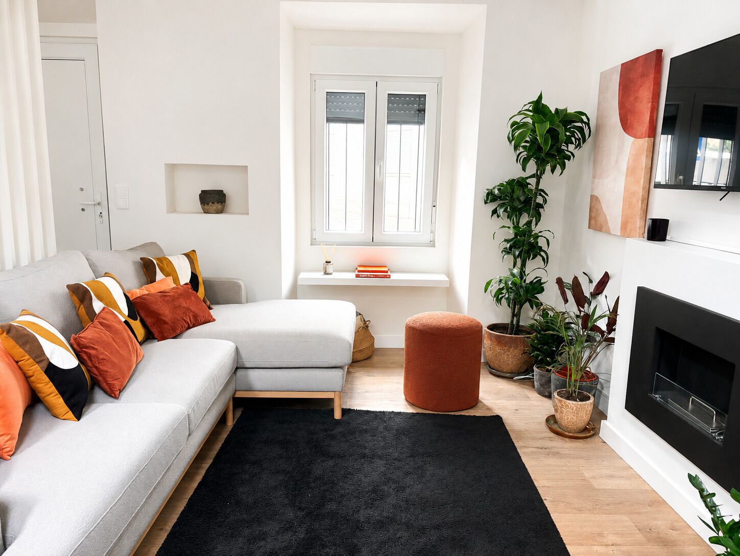 A modern living room with a sofa, ottoman, and potted plants.