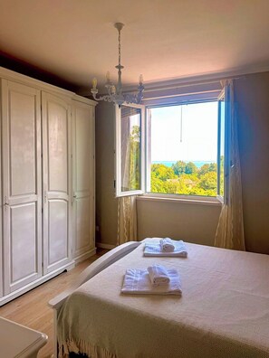 Ein Schlafzimmer mit einem großen Bett, einem Kleiderschrank, einer Chandelüster und einem Fenster mit Blick auf Grünflächen.